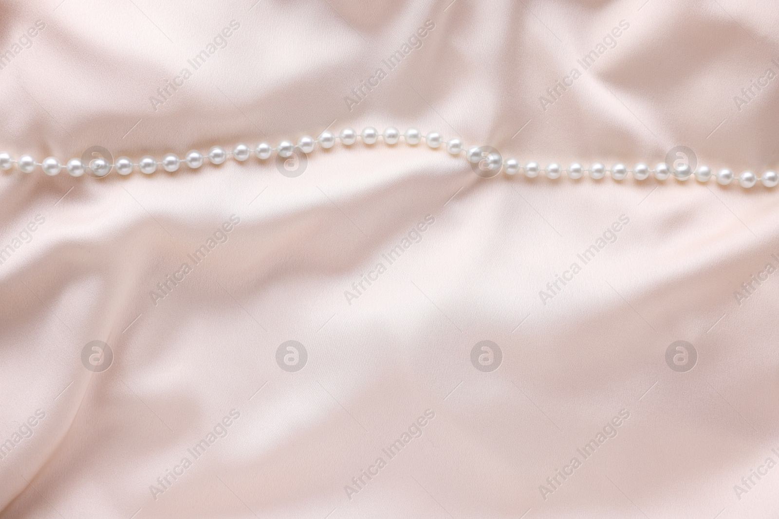 Photo of Beautiful pearl necklace on beige cloth, top view. Space for text