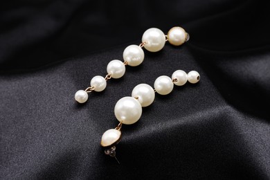 Photo of Beautiful pearl earrings on black cloth, closeup