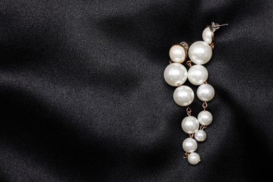 Photo of Beautiful pearl earrings on black cloth, top view. Space for text