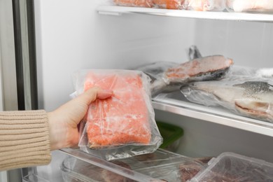 Photo of Woman taking frozen piece of salmon out of fridge, closeup