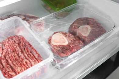 Photo of Frozen beef steaks and minced meat in containers on fridge shelf, closeup