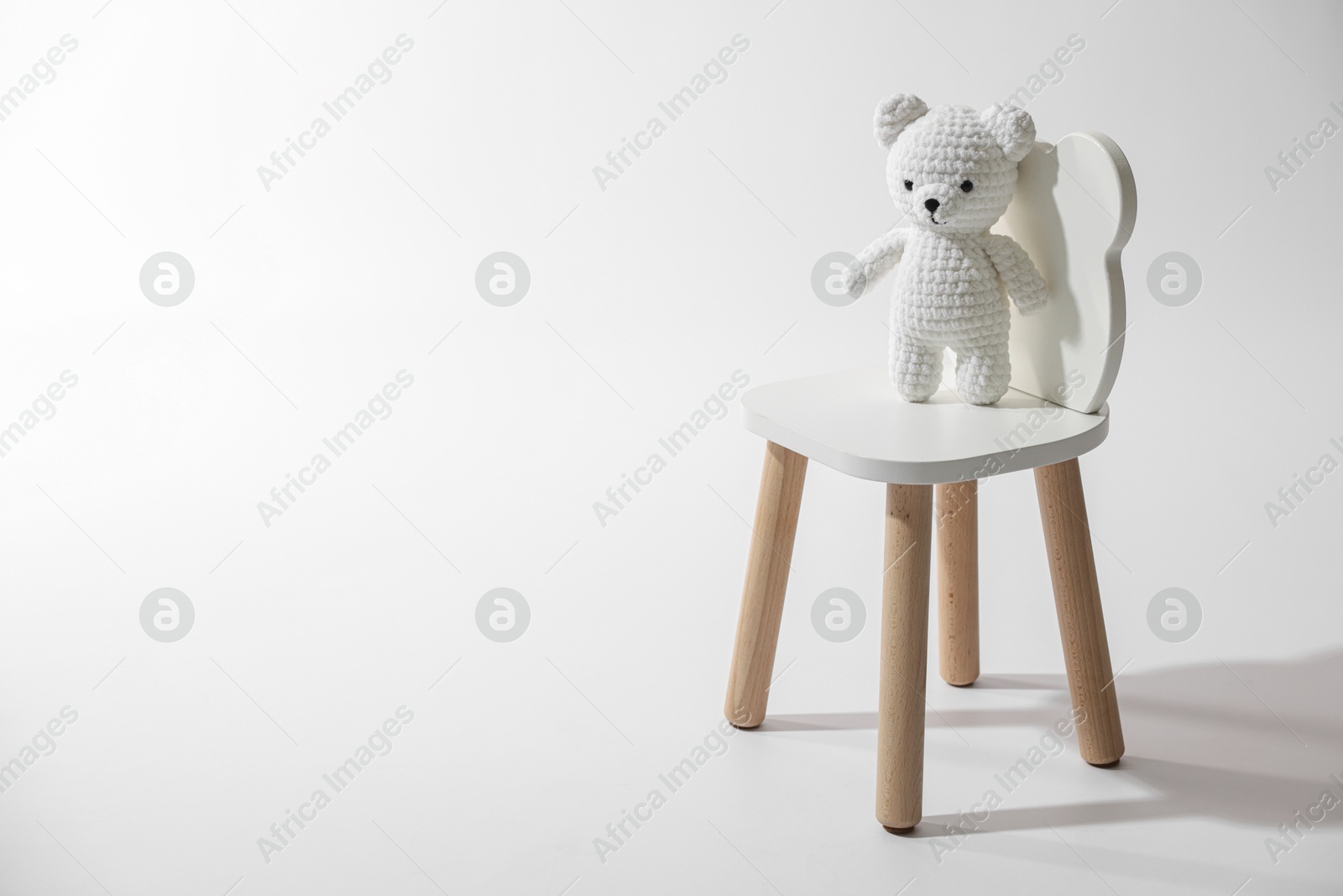 Photo of Cute crocheted bear on wooden chair against white background, space for text