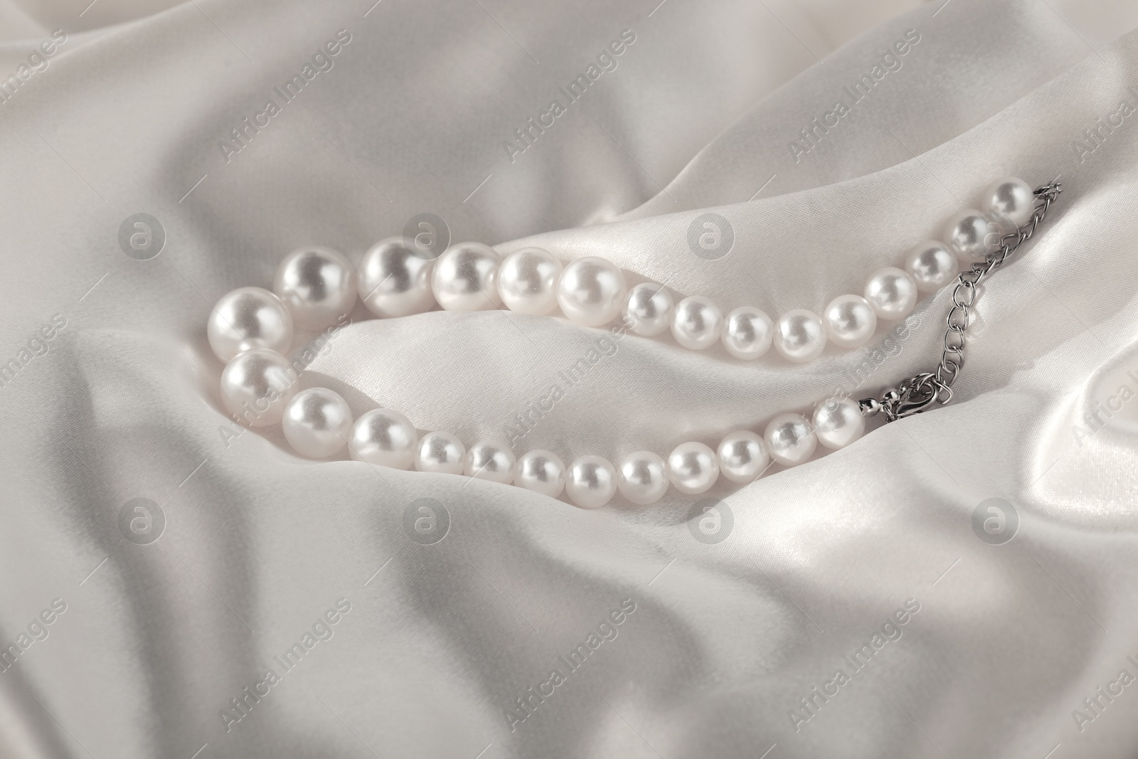 Photo of Beautiful pearl necklace on white silk, closeup