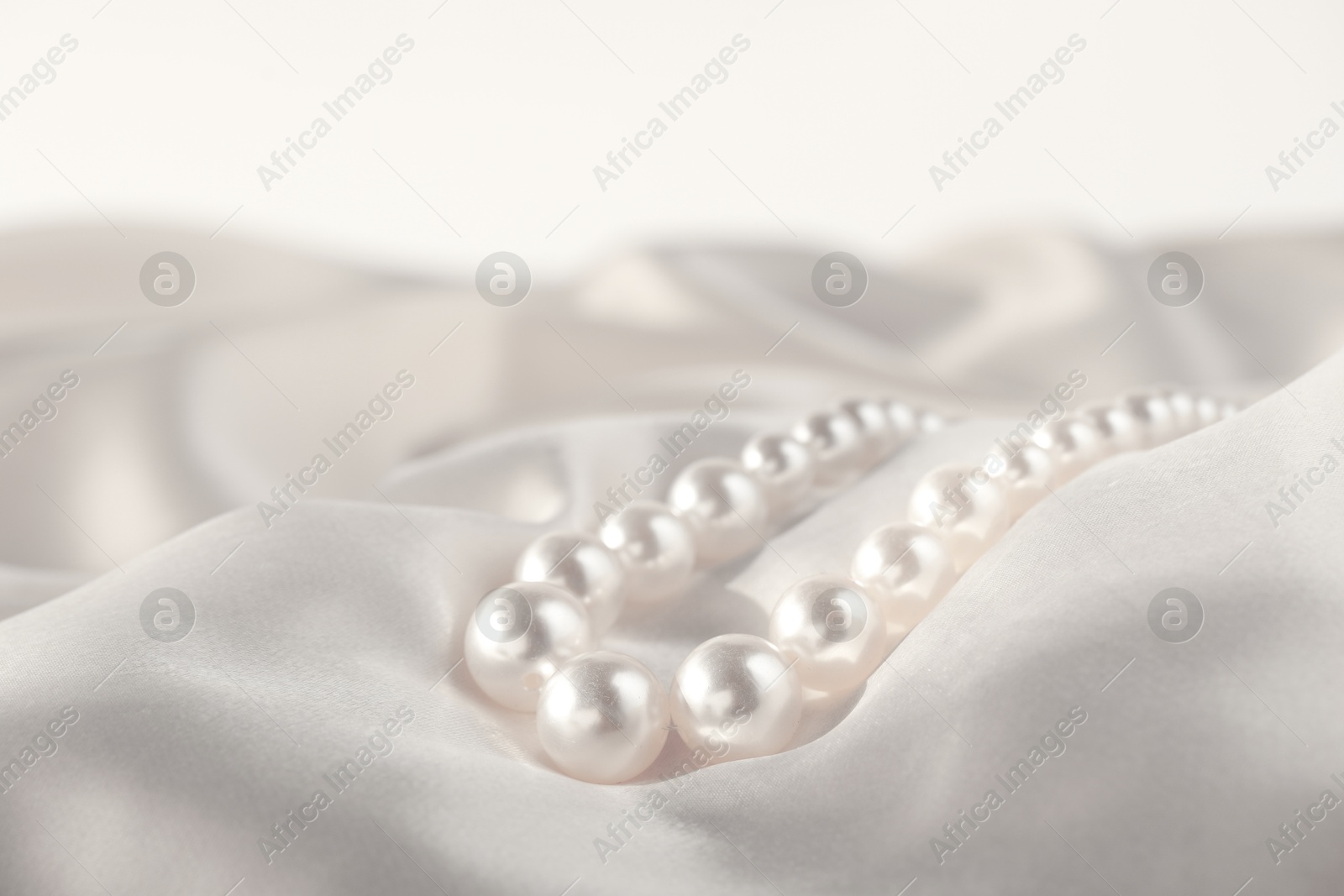 Photo of Beautiful pearl necklace on white silk, closeup