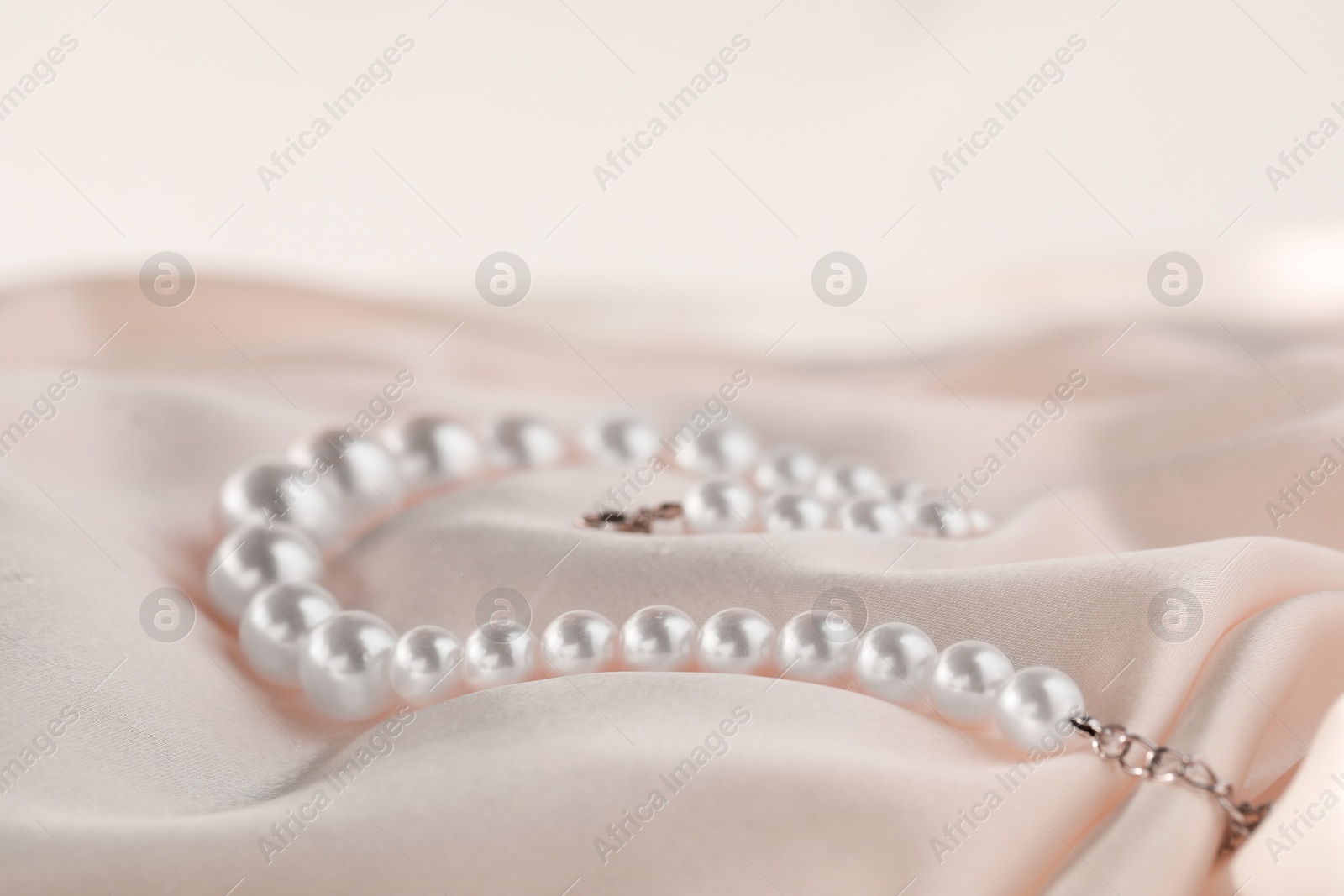 Photo of Beautiful pearl necklace on white silk, closeup