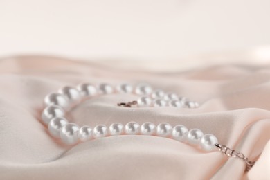 Photo of Beautiful pearl necklace on white silk, closeup