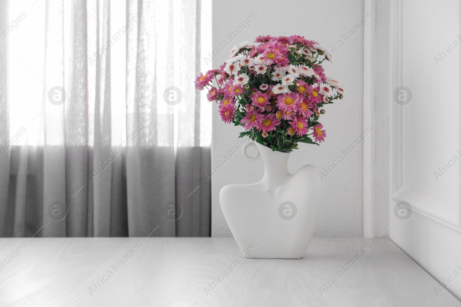 Photo of Stylish vase with beautiful flowers on white wooden table at home, space for text