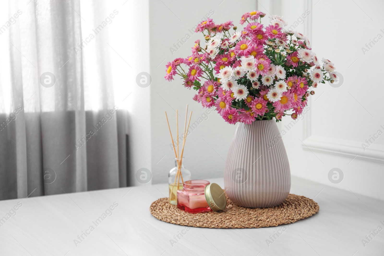 Photo of Beautiful flowers in vase, candle and reed diffuser on white wooden table at home, space for text