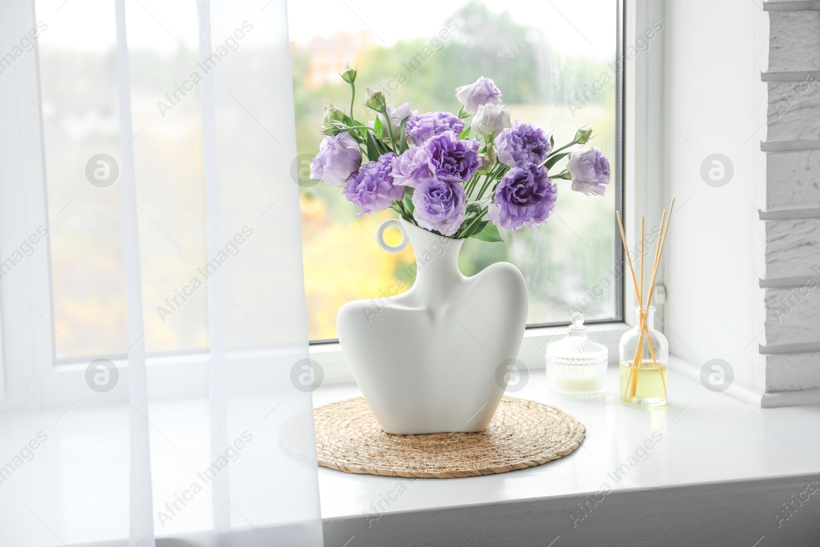 Photo of Stylish vase with beautiful flowers, candle and reed diffuser near window at home