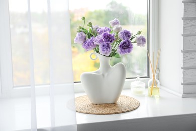 Photo of Stylish vase with beautiful flowers, candle and reed diffuser near window at home