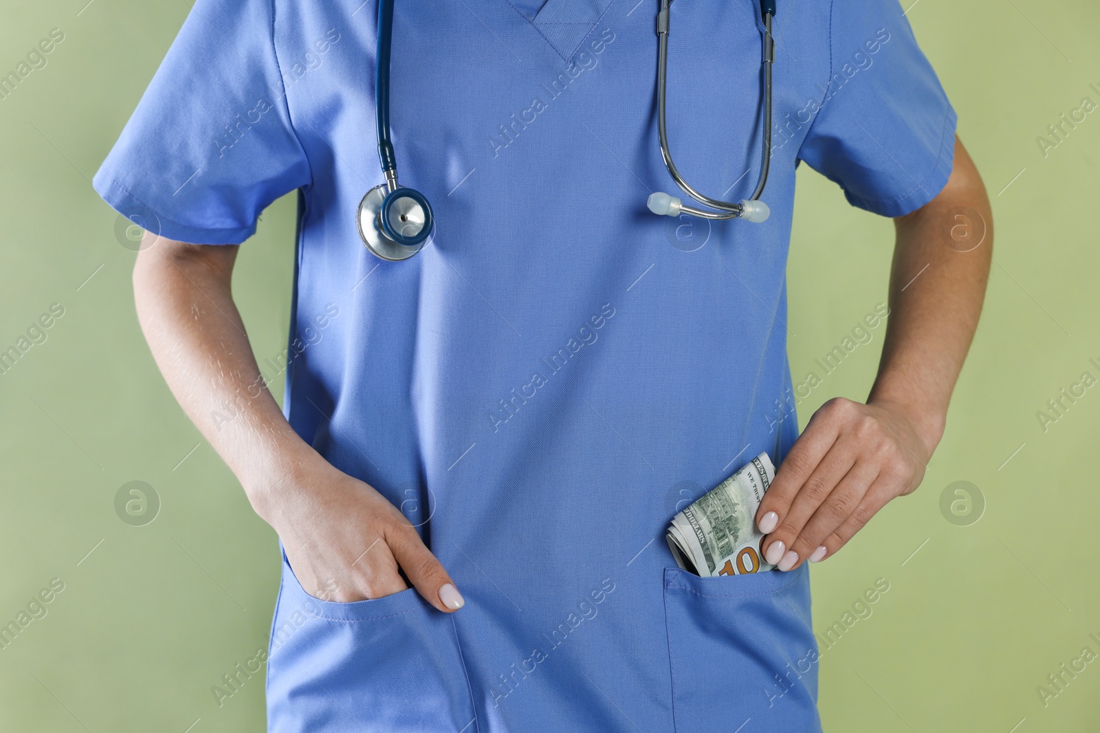 Photo of Corruption concept. Doctor putting dollar banknotes into her pocket on green background, closeup