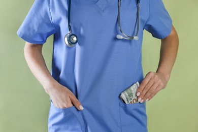 Photo of Corruption concept. Doctor putting dollar banknotes into her pocket on green background, closeup