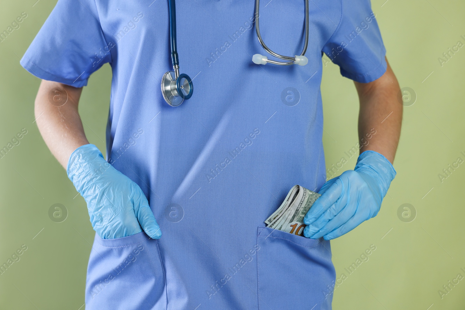 Photo of Corruption concept. Doctor putting dollar banknotes into her pocket on green background, closeup