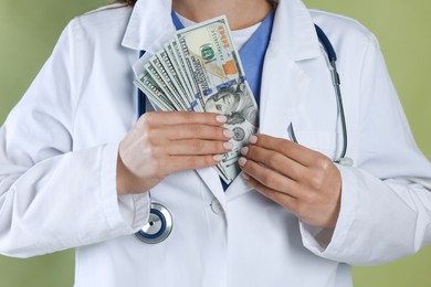 Photo of Corruption concept. Doctor putting dollar banknotes into her coat on green background, closeup