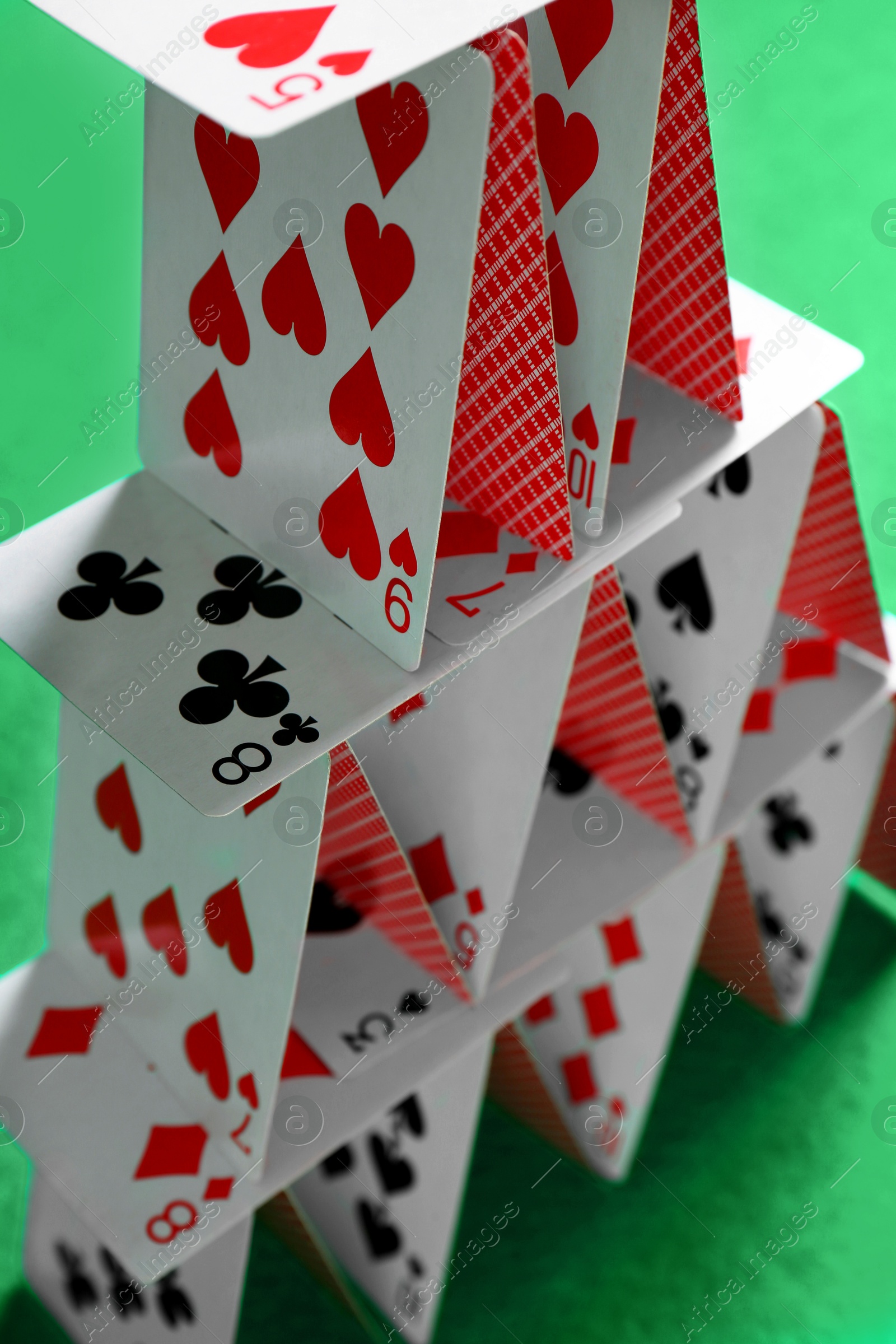 Photo of House of playing cards on green background, closeup