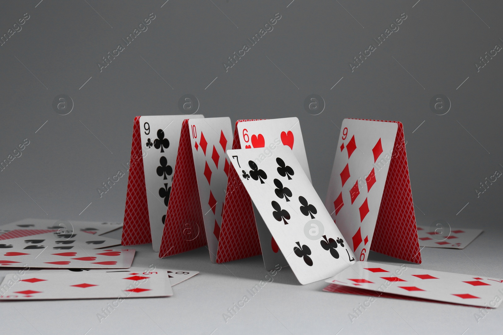 Photo of Collapsed house of playing cards on grey background, closeup