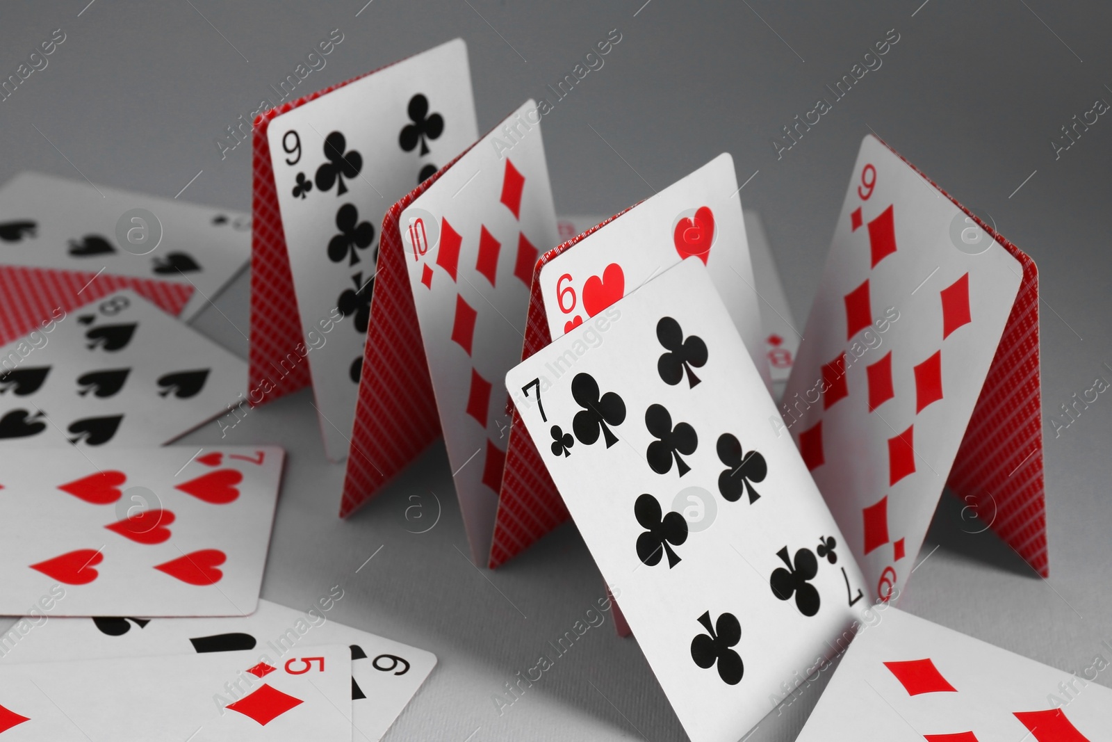 Photo of Collapsed house of playing cards on grey background, closeup