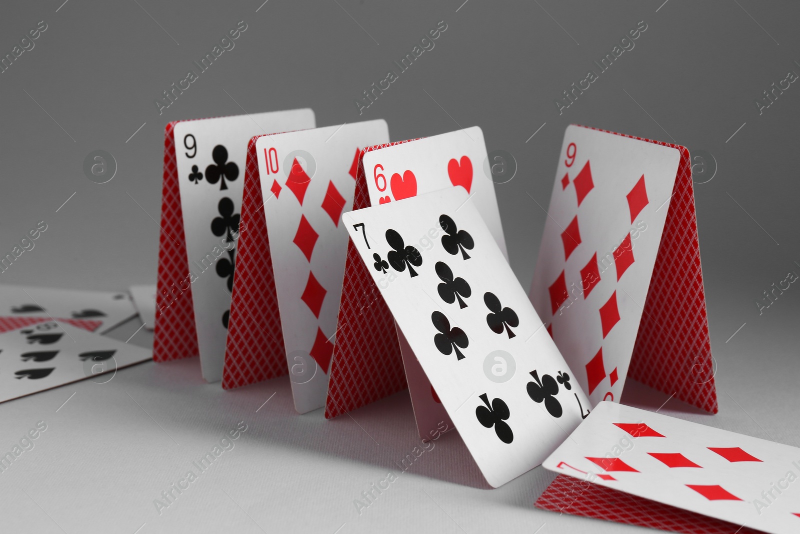 Photo of Collapsed house of playing cards on grey background, closeup