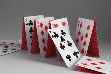 Photo of Collapsed house of playing cards on grey background, closeup