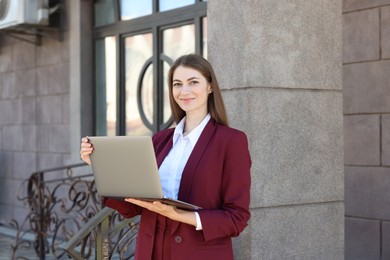 Portrait of young woman with laptop wearing stylish suit outdoors