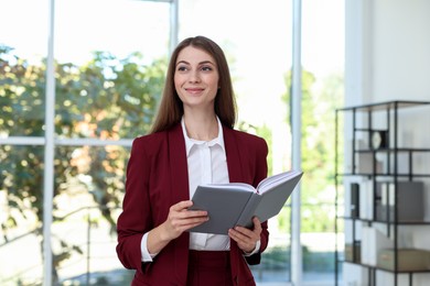 Portrait of young woman with book wearing stylish suit indoors