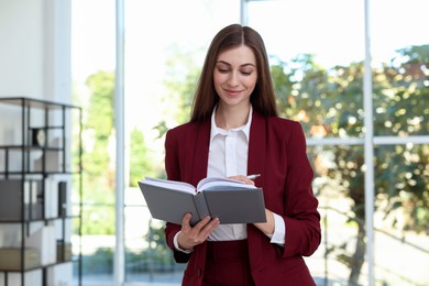 Photo of Portrait of young woman with book wearing stylish suit indoors