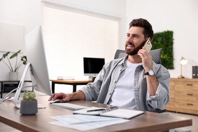 Photo of Man talking on smartphone while working at table in office