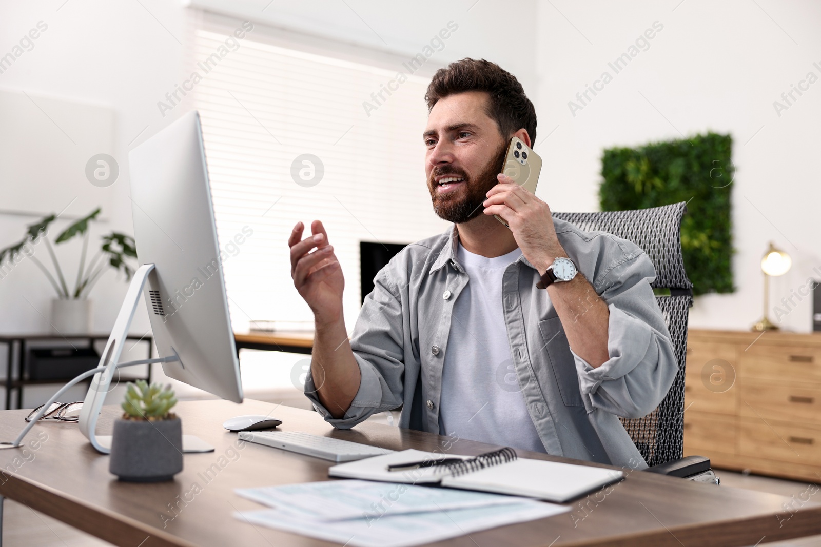 Photo of Man talking on smartphone while working at table in office