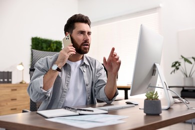 Man talking on smartphone while working at table in office