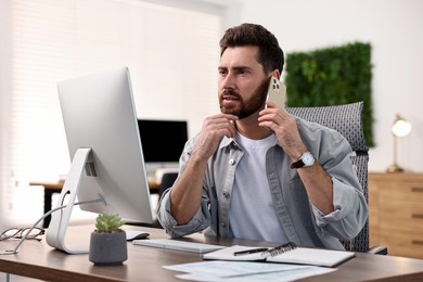 Photo of Man talking on smartphone while working at table in office