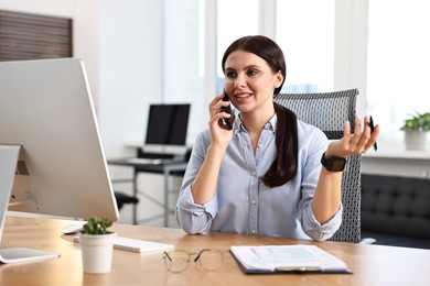 Photo of Woman talking on smartphone while working at table in office