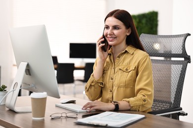 Photo of Woman talking on smartphone while working at table in office