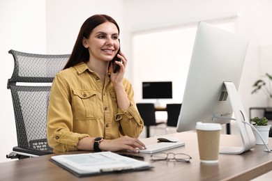 Photo of Woman talking on smartphone while working at table in office