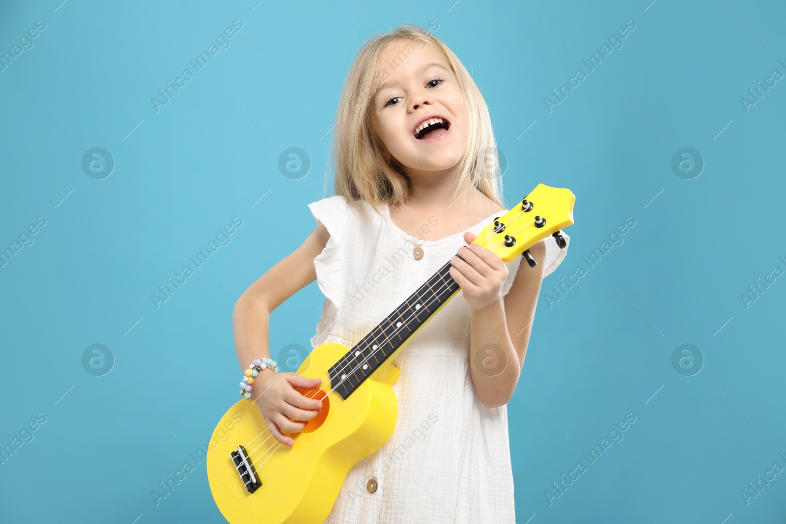 Photo of Little girl playing ukulele on light blue background