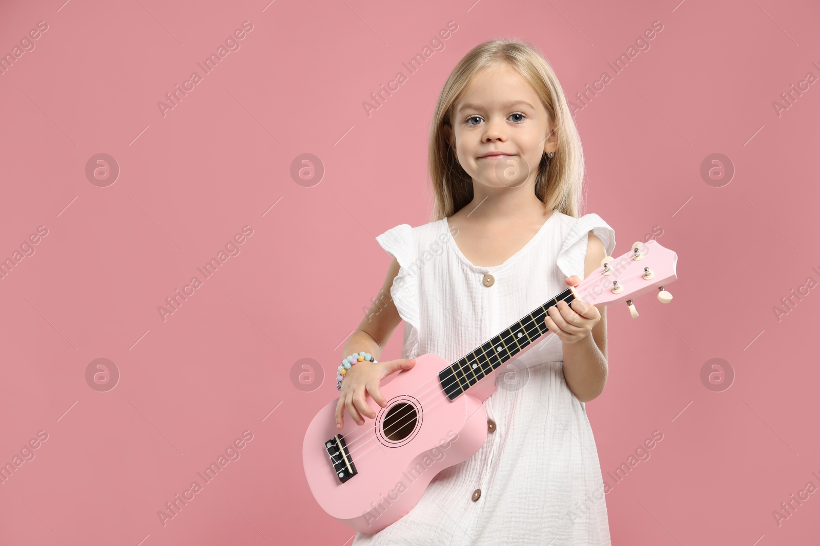 Photo of Little girl playing ukulele on pink background