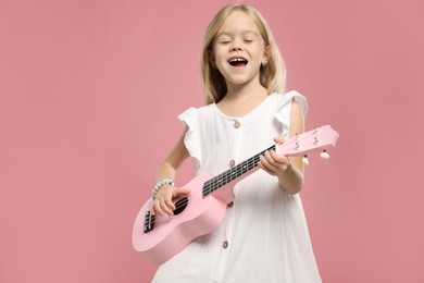 Photo of Little girl playing ukulele on pink background