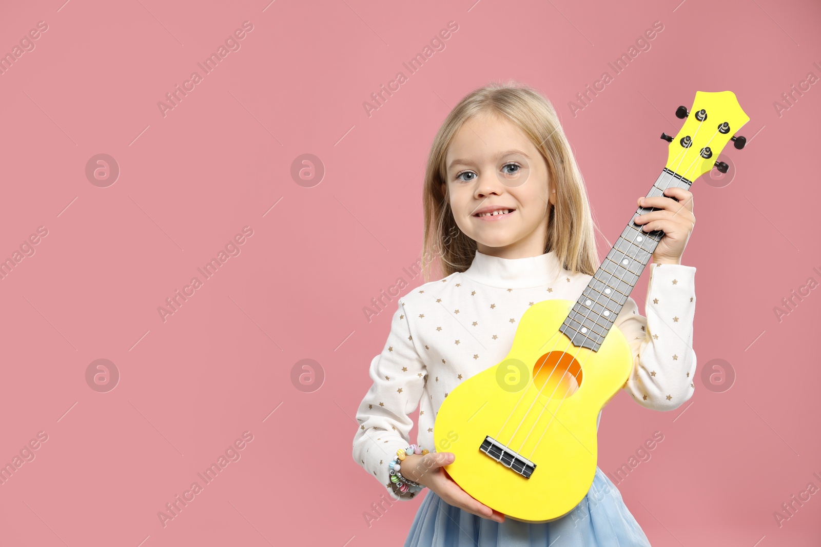 Photo of Little girl with ukulele on pink background, space for text