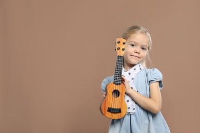 Photo of Little girl with ukulele on brown background, space for text