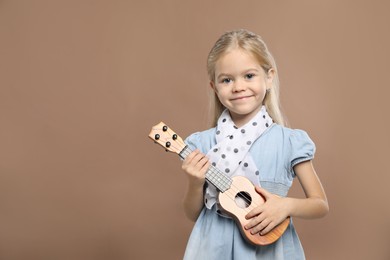 Photo of Little girl playing ukulele on brown background, space for text