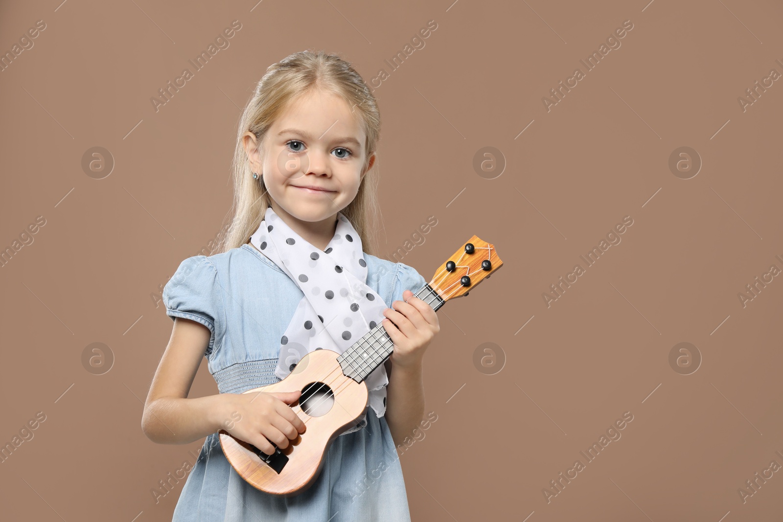 Photo of Little girl playing ukulele on brown background, space for text