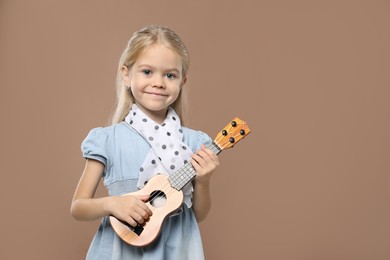 Photo of Little girl playing ukulele on brown background, space for text