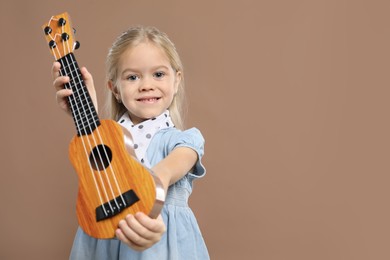 Photo of Little girl with ukulele on brown background, space for text