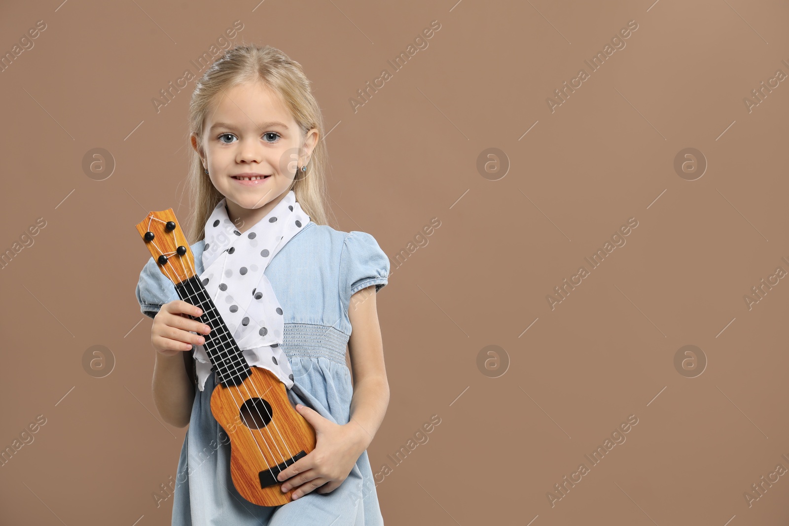 Photo of Little girl with ukulele on brown background, space for text