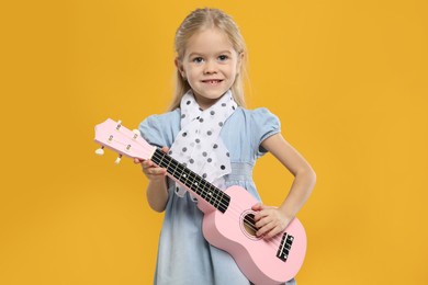 Photo of Little girl playing ukulele on orange background