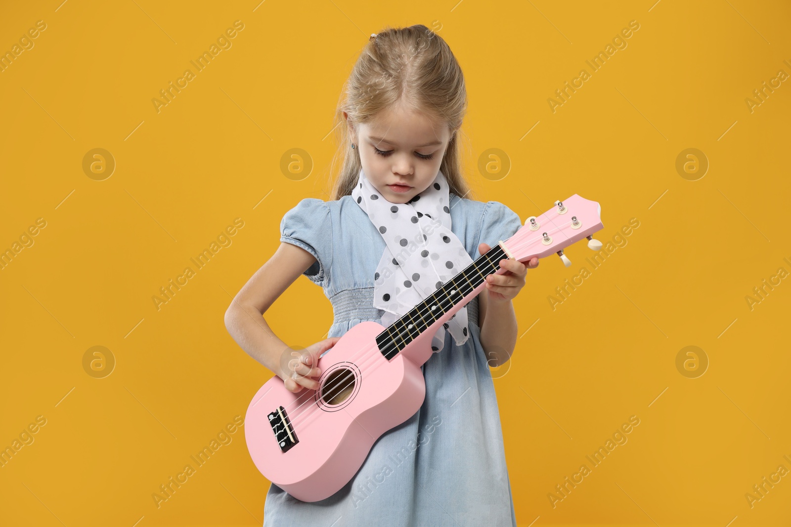 Photo of Little girl playing ukulele on orange background