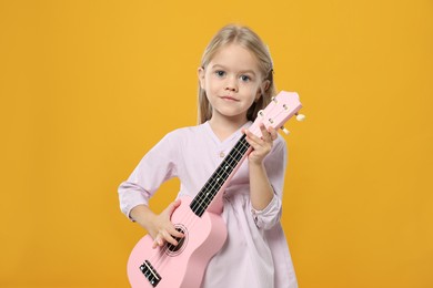 Photo of Little girl playing ukulele on orange background