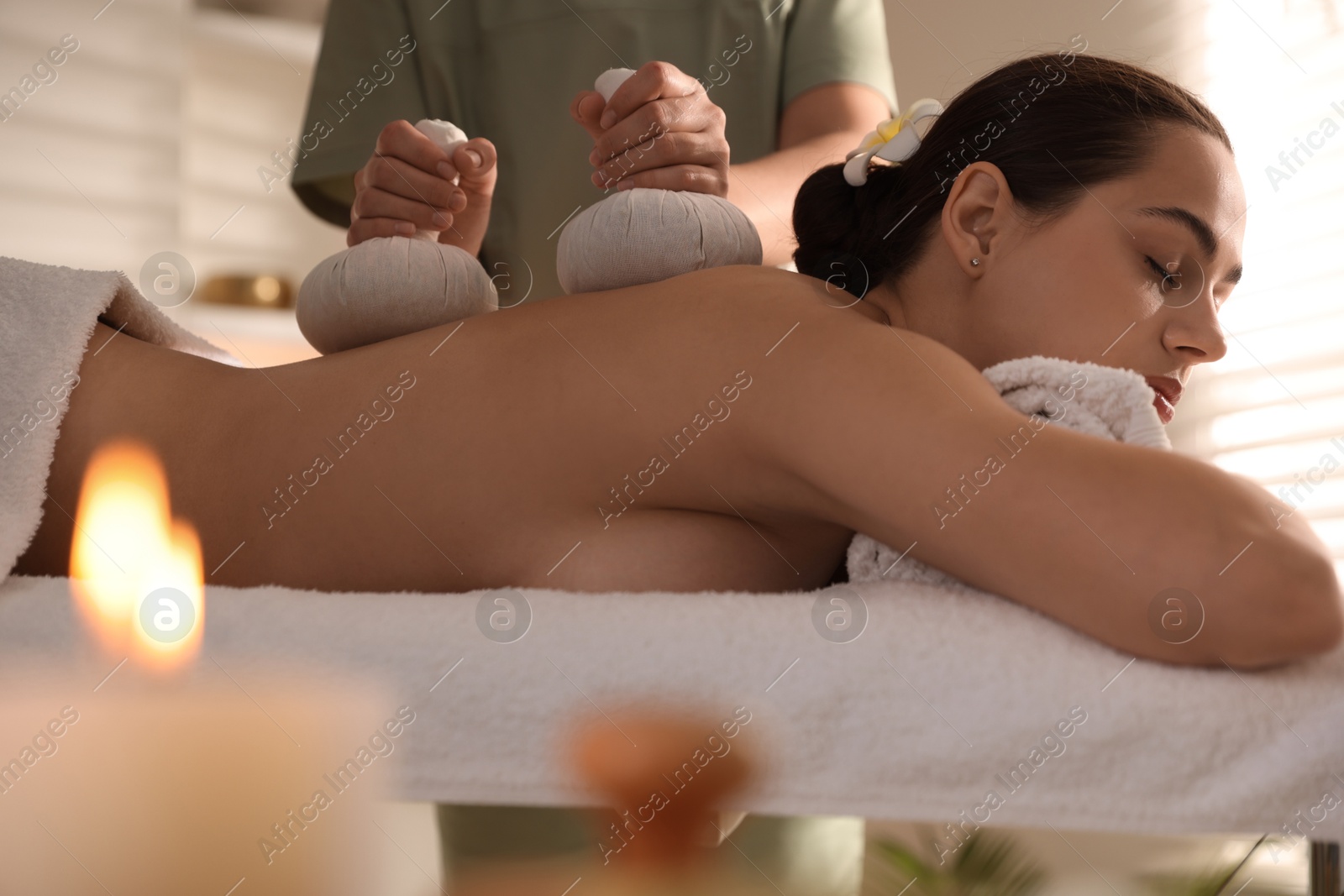 Photo of Woman receiving back massage with herbal bags in spa salon