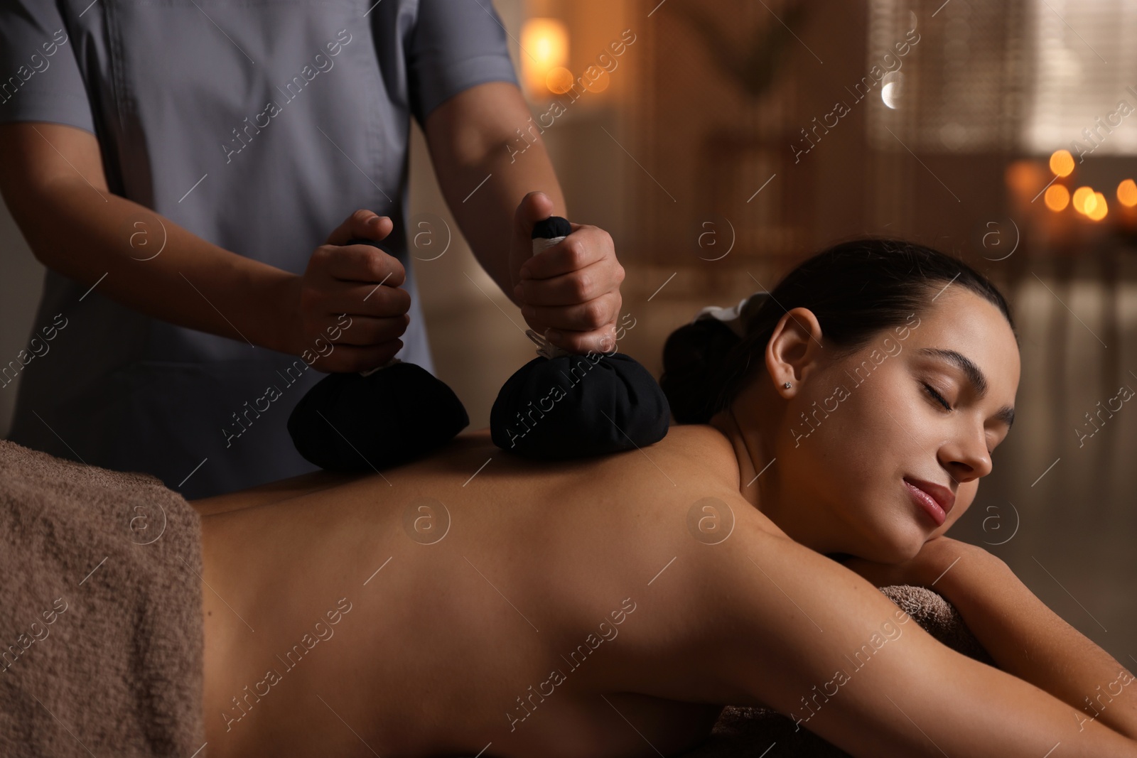 Photo of Woman receiving back massage with herbal bags in spa salon