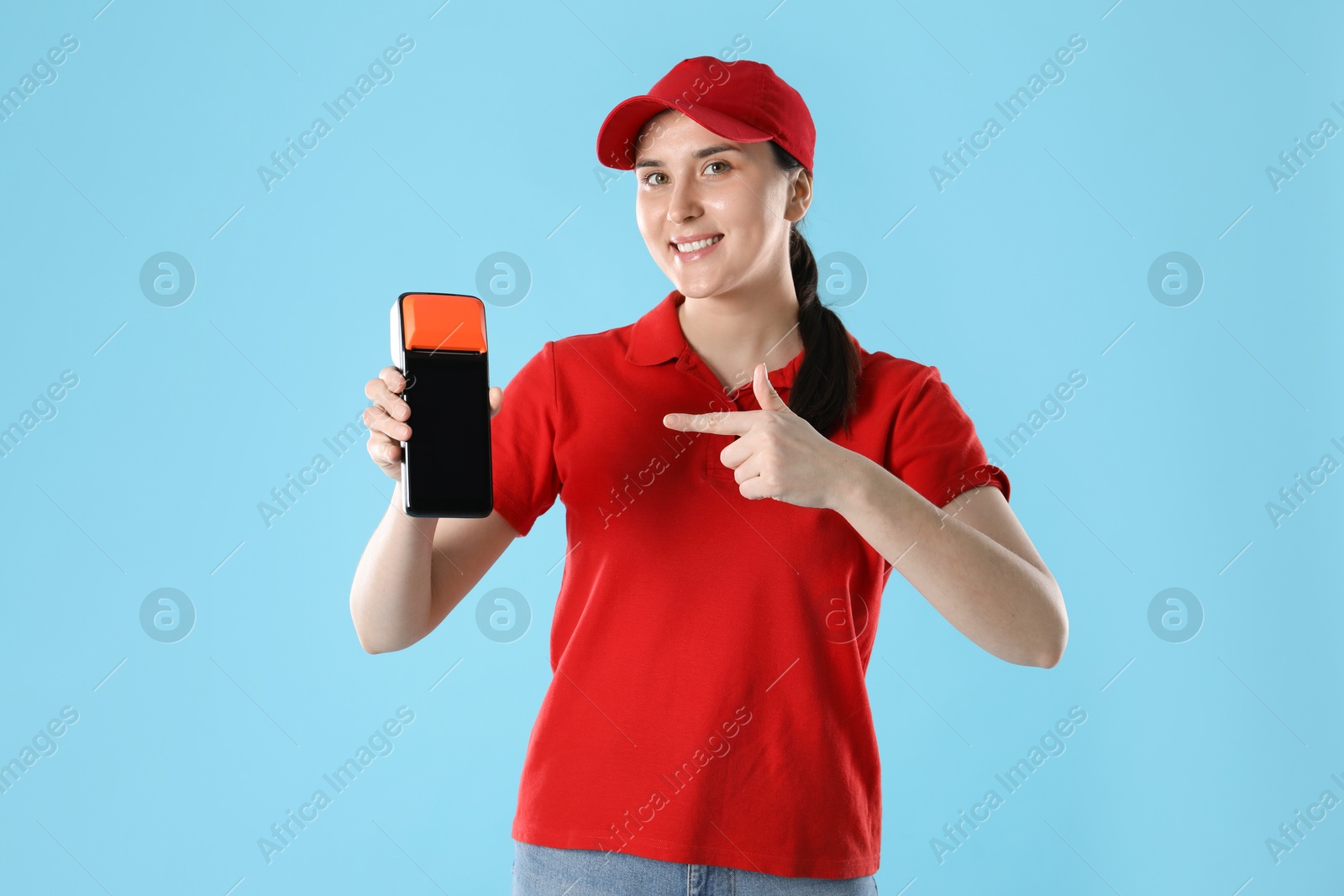 Photo of Happy courier with payment terminal on light blue background