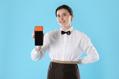 Happy waitress with payment terminal on light blue background